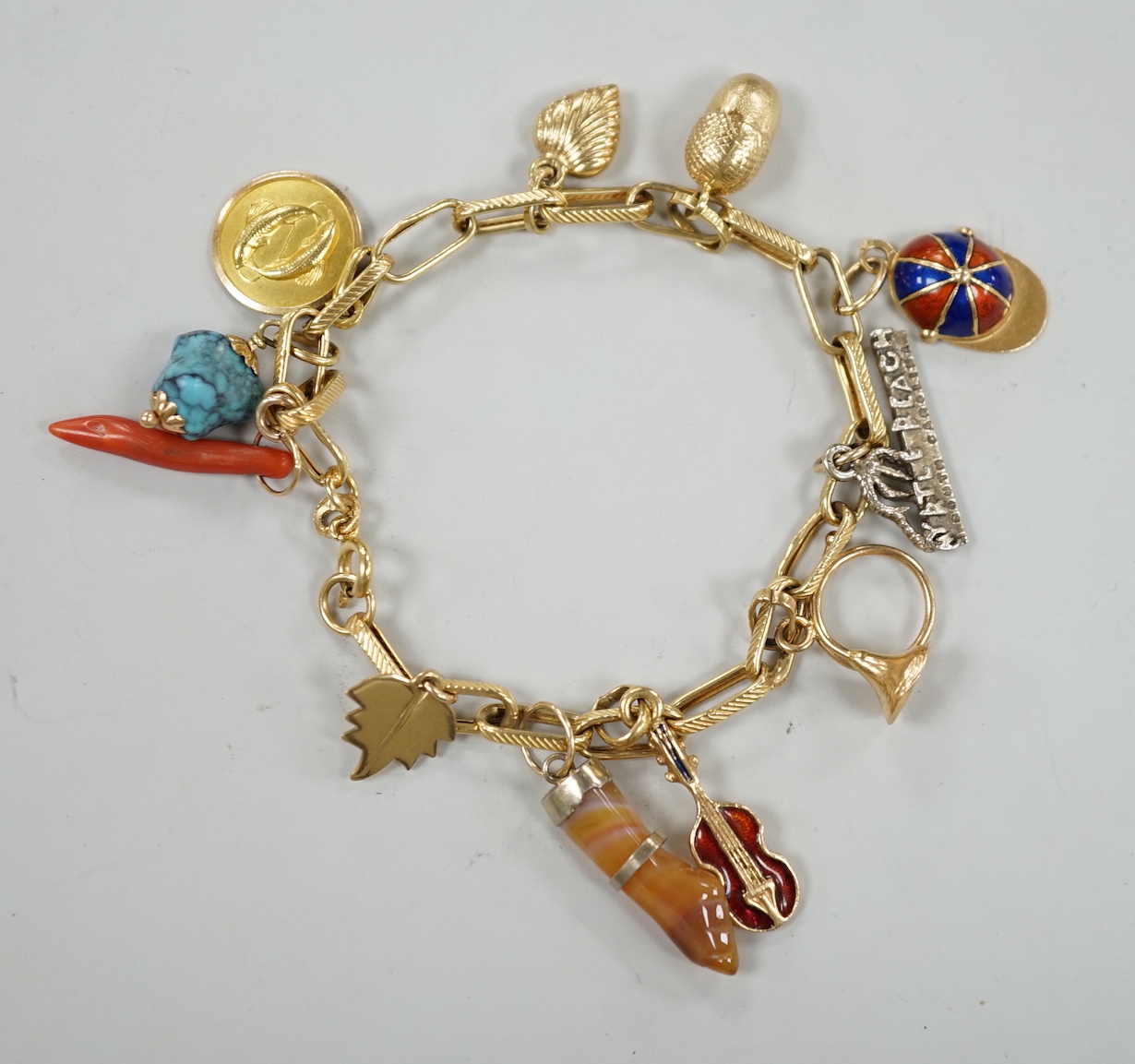 A modern Italian yellow metal charm bracelet, hung with eleven assorted charms, including 750 and enamel jockey cap, agate clasped hand and 750 acorn